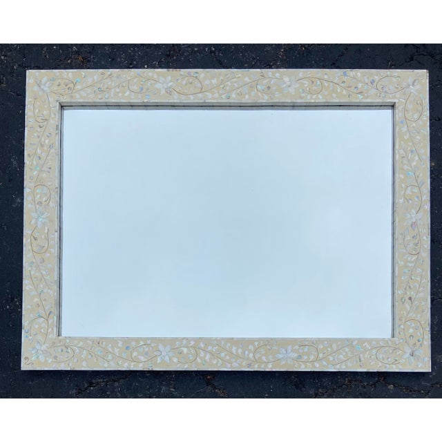 Elegant wall mirror featuring an intricate, hand-crafted mother-of-pearl floral vine inlay on a pale, buttery cream...