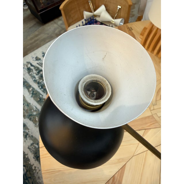 A sculptural Stilnovo table lamp featuring a long brass arm, a black metal shade, and an ivory accent above the shade. Its...