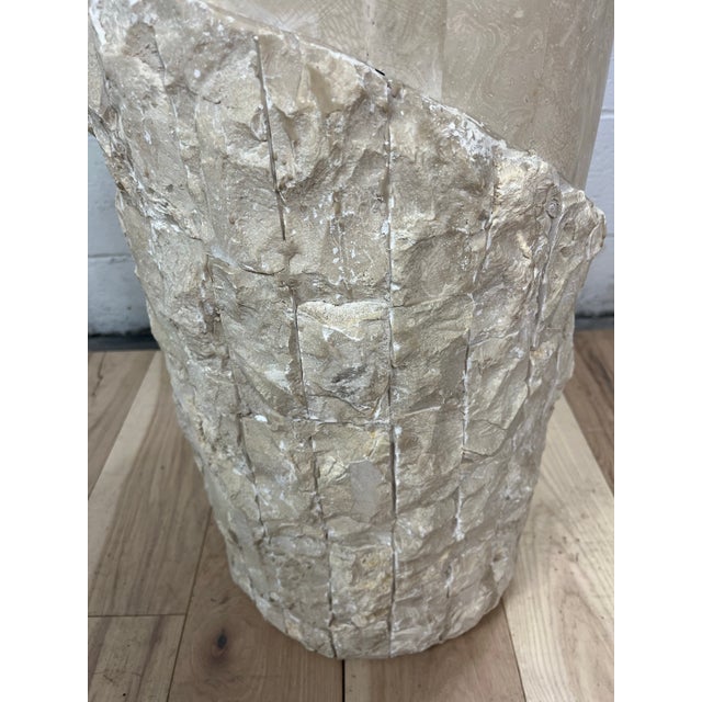 Sculptural vintage pedestal featuring a cylindrical silhouette clad in tessellated stone in warm cream and sand tones. A...