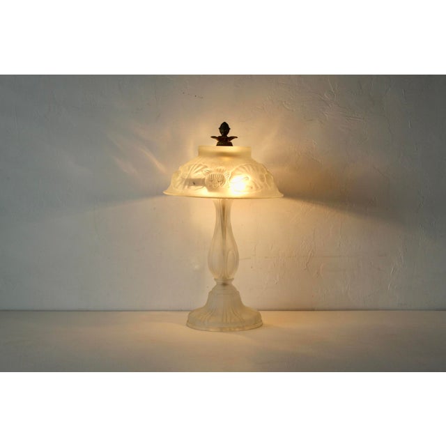 Vintage Art Nouveau-style frosted glass table lamp featuring a molded floral relief shade and matching frosted glass base....