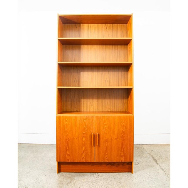 Functional compact bookshelf in teak. Bottom section offers cabinet doors with solid teak handles. The above bookshelf...