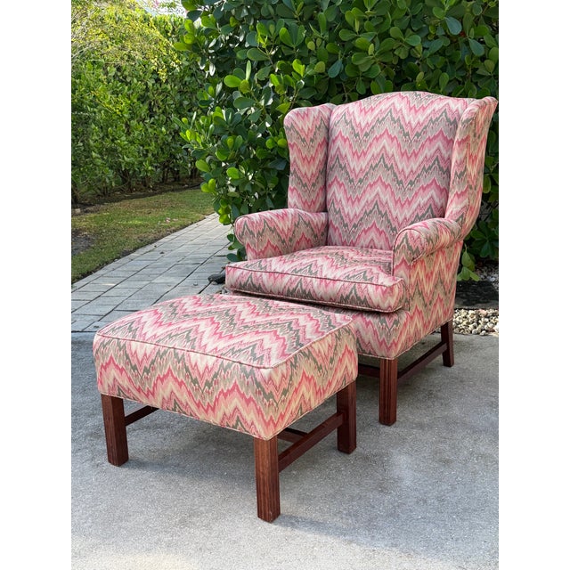 Vintage American flamestitch wingback chair and matching ottoman, featuring a vibrant coral, pink, cream, and olive...