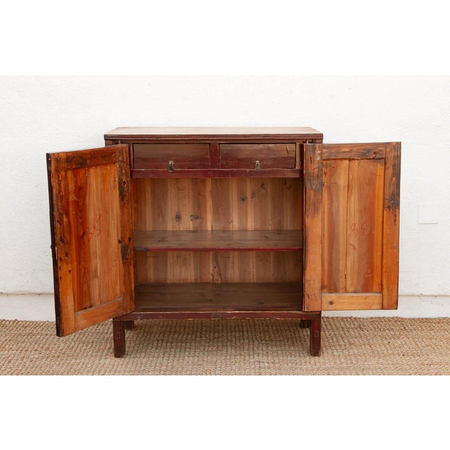 Two recessed door panels finished in a saturated red sit within a darker brown-black lacquered frame on this cabinet,...