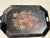 The hand-painted toleware features a colorful, worn floral bouquet in the center of a black metal tray with cutout handles...