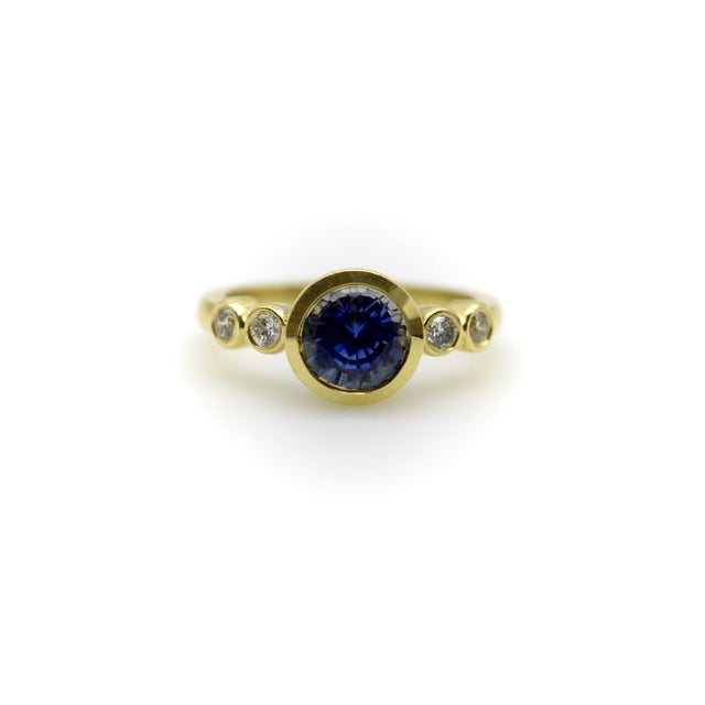 This 18k gold ring’s center stone is a natural vibrant medium-blue sapphire. The stone has a depth that draws you in and...