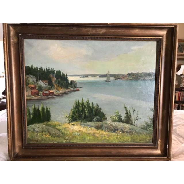 A large landscape painting of a lake and the houses and trees surrounding the lake. The painting is signed in the bottom...