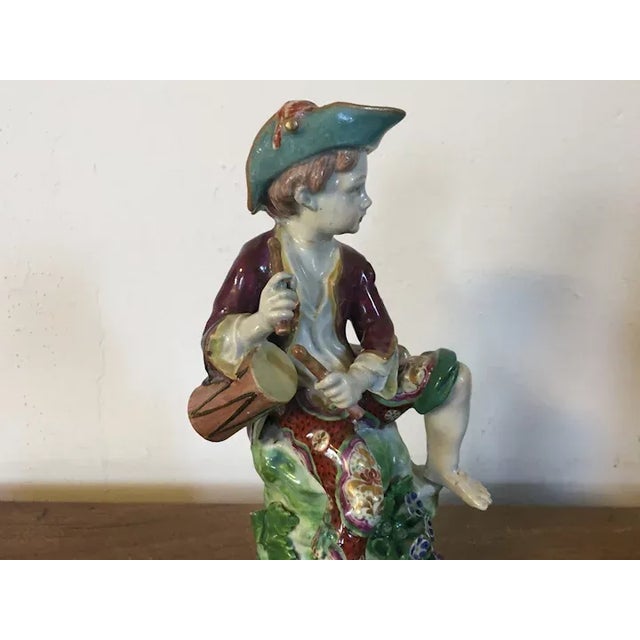 Antique 18th century Bow porcelain figure of a drummer boy. The figure seated on a grassy mound and dressed in a bright...