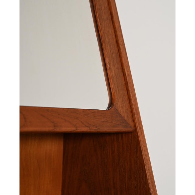 Teak wall-mounted cabinet with an opening mirror door, internal storage, and a double shelf. Scandinavian design, 1960s....