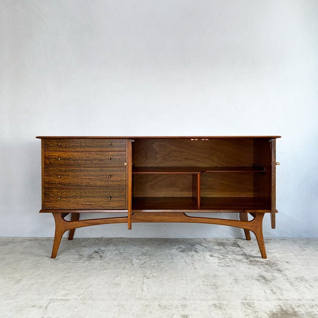 A sideboard by Alfred Cox, the case veneered in strongly figured walnut across the top, sides, drawer fronts and doors,...