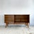 A sideboard by Alfred Cox, the case veneered in strongly figured walnut across the top, sides, drawer fronts and doors,...