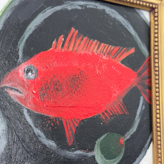 An original still life painting depicting a brilliant scarlet red fish alongside a single green olive in a black pan. The...