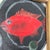 An original still life painting depicting a brilliant scarlet red fish alongside a single green olive in a black pan. The...