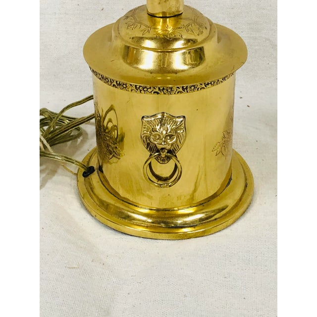 Oval brass table lamp with lion head knockers on each side. Engraved design embellishes the front, back and around the top.