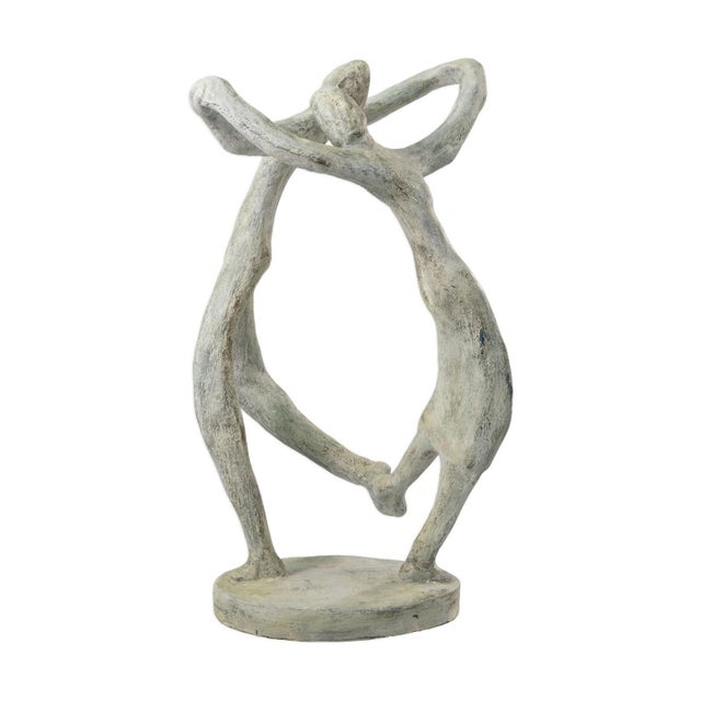 A carved stone sculpture depicting two abstracted figures in a dancing pose. The figures are shown standing on a circular...