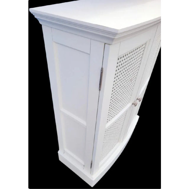 An oversized vintage cane and wood white bathroom wall medicine storage cabinet. The cabinet features 2 doors with cane...