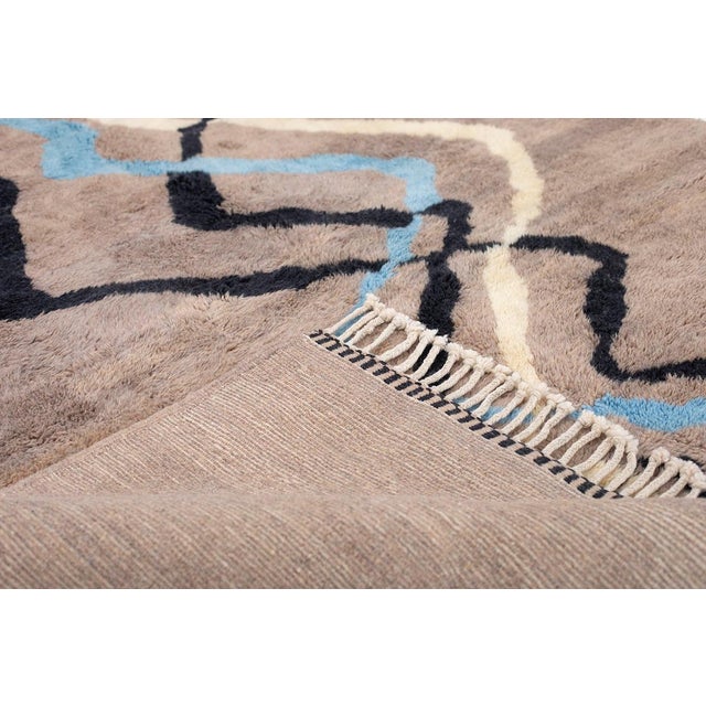 Movement captured in wool, line by winding line. Three sinuous ribbons — ivory, sky blue, and midnight black — meander...