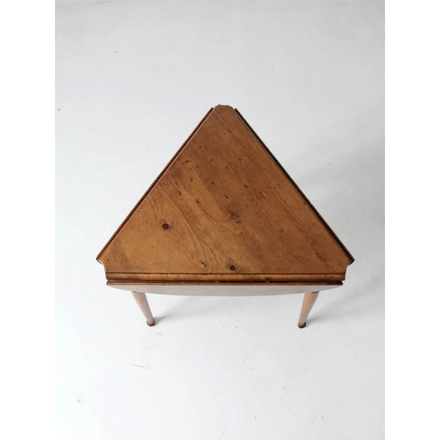 This is a mid 20th century wooden end table. The triangular table features drop leaves that open to a rounded table top....
