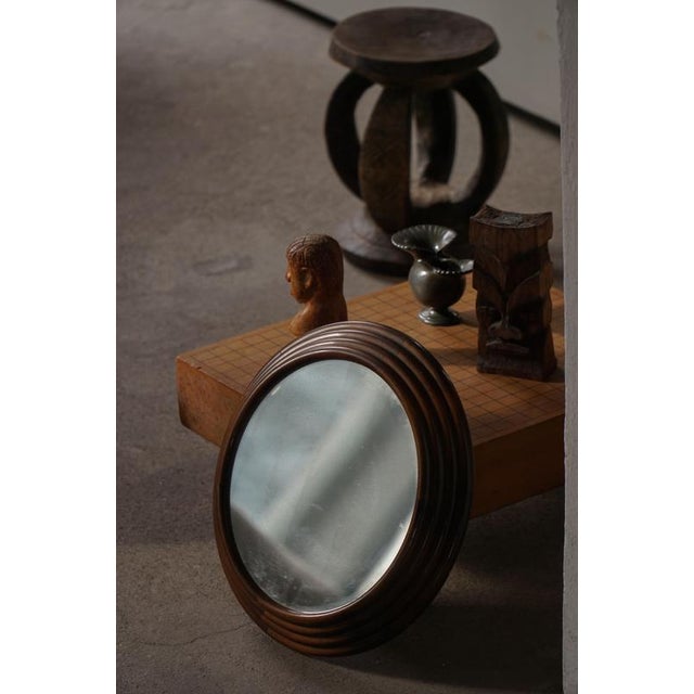 A round small and decorative wall mirror featuring a sculptural wooden frame with softly stepped, carved detailing. The...
