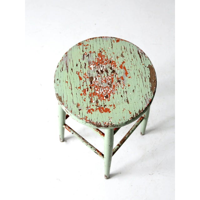 This is a painted wooden stool circa dating to the early 20th century. The wooden round seat counter stool features layers...