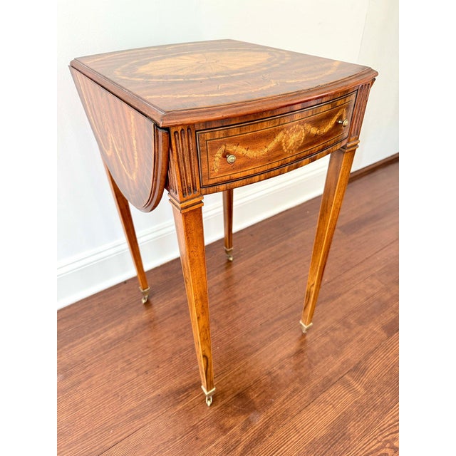 A single drawer Maitland-Smith drop leaf side table featuring a refined oval form, slender tapered legs, and classic...