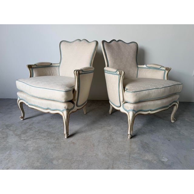 An elegant pair of vintage Hollywood Regency bergère armchairs inspired by classic French Louis XV design. These...