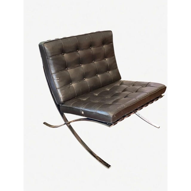 Iconic Barcelona chair by Ludwig Mies van der Rohe, featuring a sleek polished chrome X-frame base and deep tufted dark...