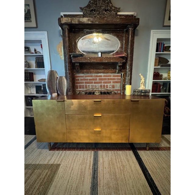 A 1960s aurum-finished media cabinet defined by clean mid-century lines, original brass hardware, and timeless...