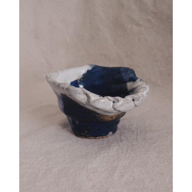 A small hand built ceramic bowl with an organic, sculpted form. The shape feels pinched and slightly irregular, with a...