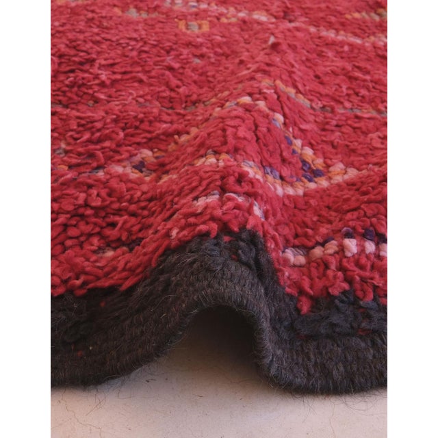 This vintage Moroccan rug showcases traditional Amazigh craftsmanship with a striking red field, likely colored using...