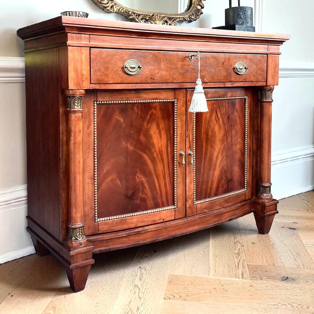 Elegant bow front cabinet featuring stunning crotch mahogany veneer, rich warm tones, and refined antique gold accents...