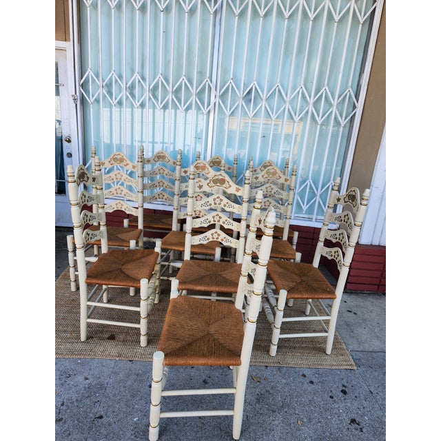 Italian Hand-painted set of ten dining chairs has a cream-colored wood frame with gold-toned accents. Each chair features...