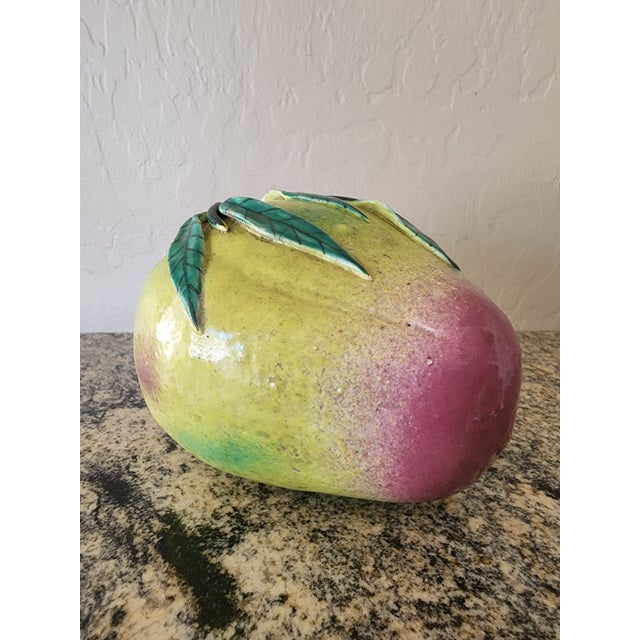 A large Chinese altar fruit modeled as a ripening peach, glowing chartreuse green with a soft raspberry blush at the tip....