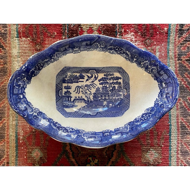 Antique Blue Willow footed oval serving dish featuring a blue transfer chinoiserie pattern on the interior. Made by...