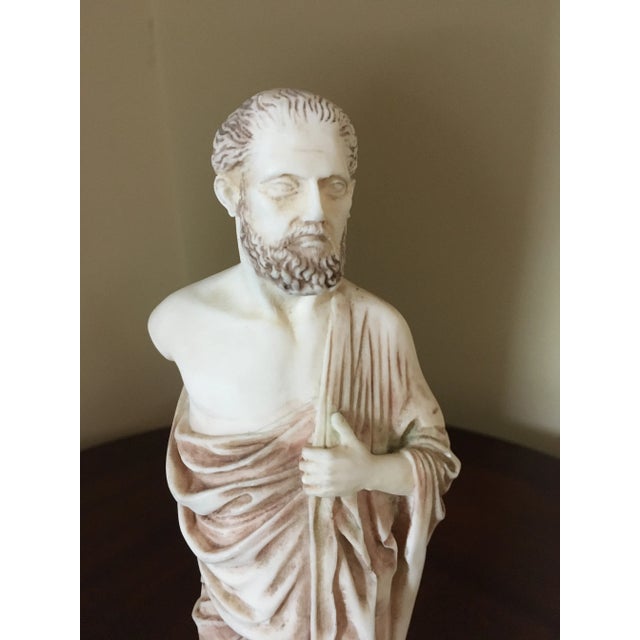 A statue of Hippocrates handmade in alabaster. It is white with intricate light brown shades for detail. It is skillfully...