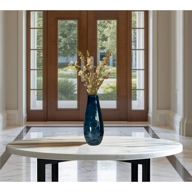 This 14 ¾-inch tall by 7-inch wide hand-blown art glass vase is crafted in a striking deep teal or petrol blue hue that...