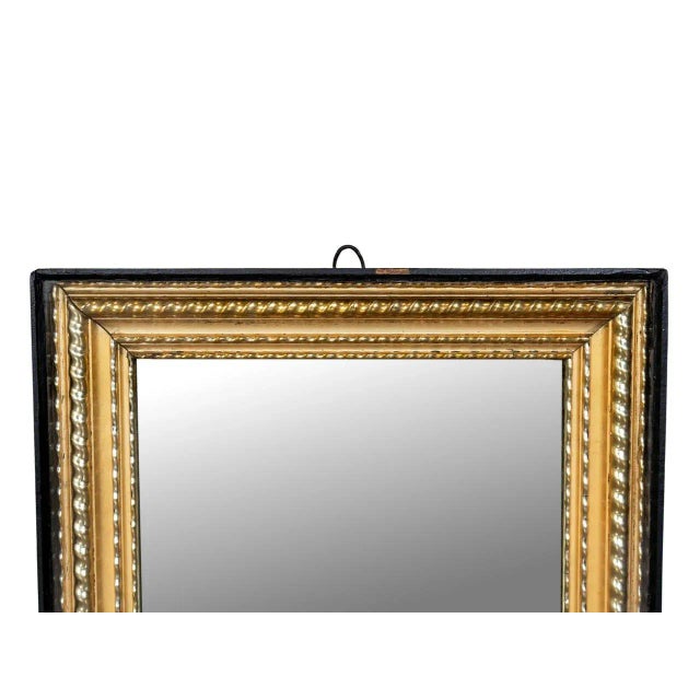 Antique wooden mirror with ornate rectangular frame. Intricate detailing with gilded gold finish and black trim.