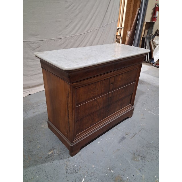 A handsome 19th-century French walnut commode featuring a substantial white marble top and beautifully figured bookmatched...