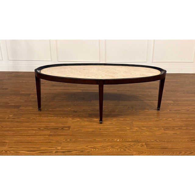This is the Winthrop Oval Cocktail Table by Maitland - Smith. It features a stone top, dark walnut wood frame and metal...