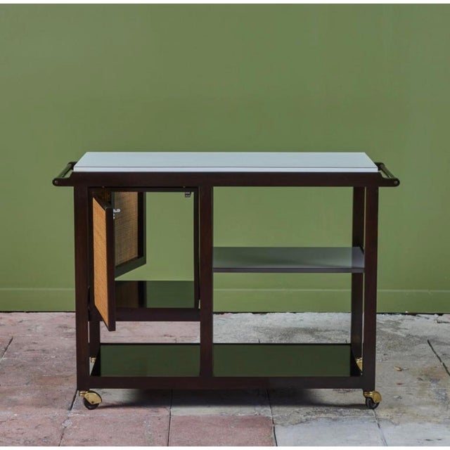 An ebonized bar cart by Edward Wormley for Dunbar, USA, c.1960s. The cart features a white laminate flip top surface with...