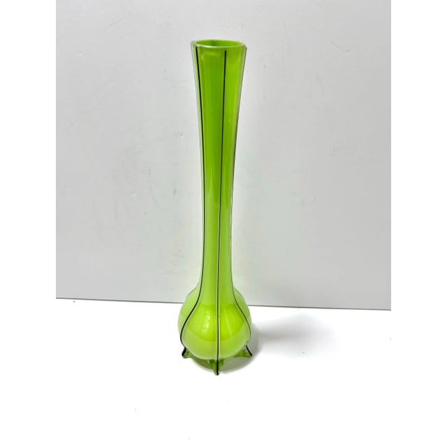 A striking 1980s hand-blown art glass vase in a vibrant green tone with black accents. The elongated silhouette and...