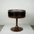 This charming chocolate brown lacquered circular Space Age side table with metal tulip base and glass top has been...