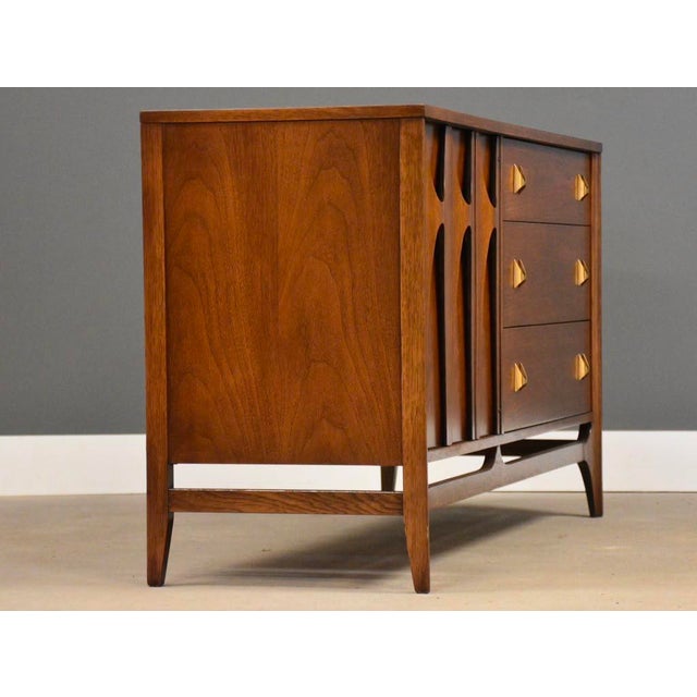 A mid century modern walnut three drawer dresser credenza with swooping walnut and brass arch details made by Broyhill...