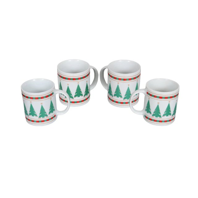 A set of four white ceramic coffee mugs. Pop art Christmas tree icons decorate the sides, framed above and below with a...