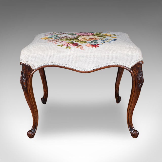 This is an antique fireside footstool. An English, needlepoint over walnut lounge stool, dating to the early Victorian...
