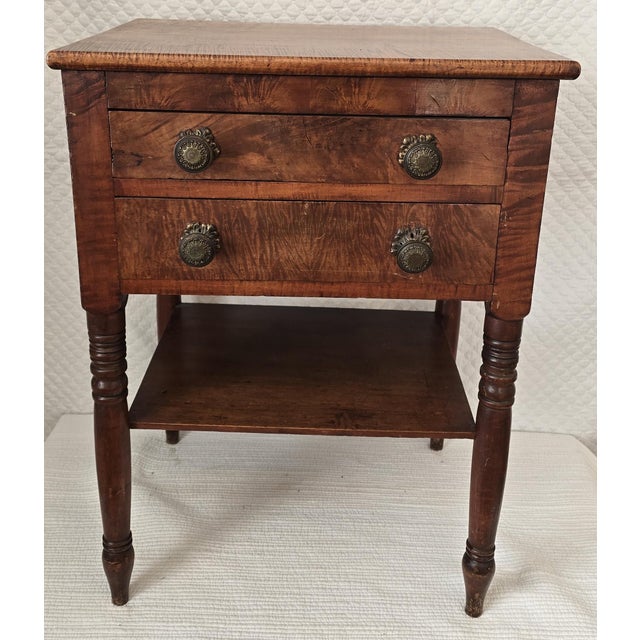 An early 19th century American Federal period two-drawer stand crafted in figured maple, displaying strong tiger grain...