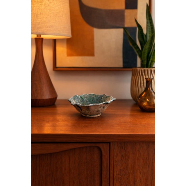 Hand-thrown studio pottery bowl featuring a sculptural, petal-like rim and richly carved interior decoration. The bowl is...