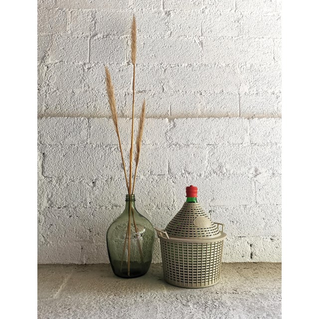 This green glass demijohn/wine carboy in a gray plastic basket was manufactured in Italy in the 1960s and imported to...