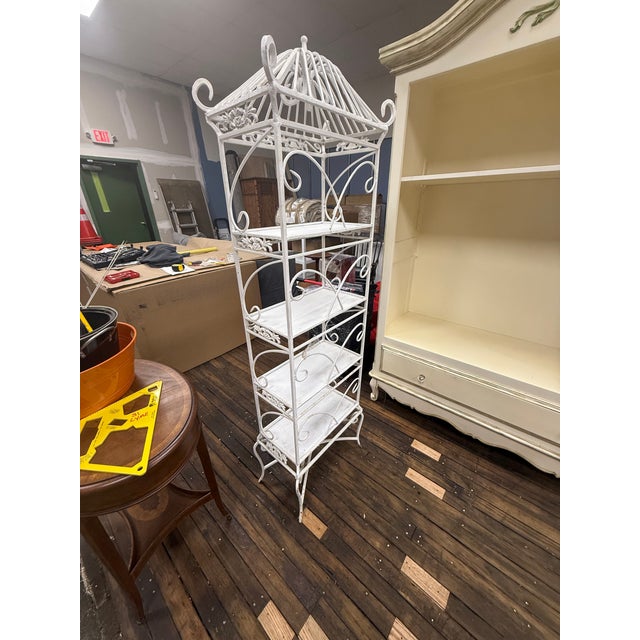 A striking five-tier wrought iron étagère featuring a dramatic pagoda crown finial, ornate scrollwork uprights, and...