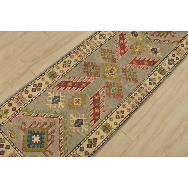 A tribal Caucasian Kazak runner hand-knotted with fine wool on a cotton foundation. This rug features geometric motifs set...