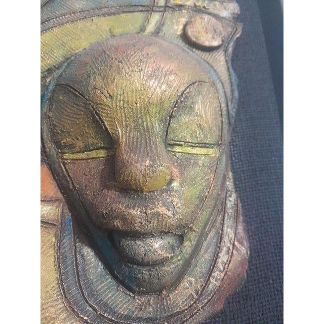 Ceramic wall art by Jamaican artist Everard Powell, featuring two stylized faces in shimmering tones of gold, turquoise,...